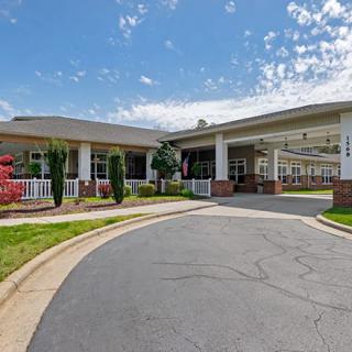 A large building with a driveway leading to its entrance, surrounded by well-maintained landscaping under a partly cloudy sky.