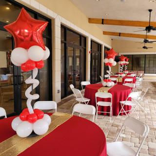An outdoor party setup with red and white balloon decorations, tables, and chairs.
