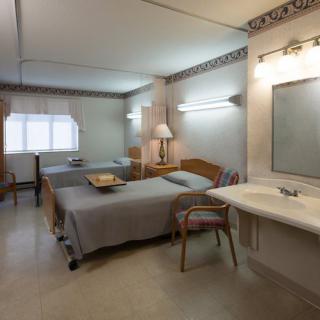 A cozy bedroom with two beds, a lamp, and a mirror above a sink.