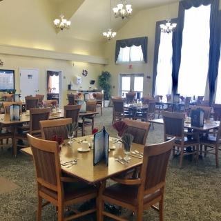 A spacious dining room with neatly arranged tables and chairs, illuminated by elegant chandeliers.