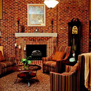 A cozy living room with a brick wall, featuring a fireplace and comfortable armchairs.