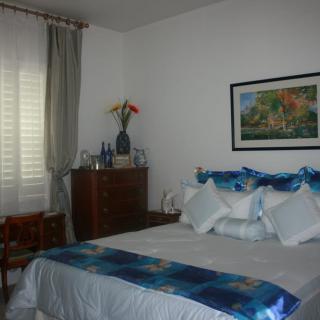 A cozy bedroom with a neatly made bed, decorated with blue accents and a painting on the wall.