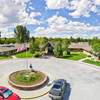 A serene community setting featuring a circular flowerbed and flags, surrounded by residential buildings under a clear blue sky.