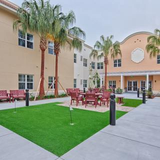 A spacious courtyard featuring palm trees, artificial grass, and outdoor seating surrounded by a building.