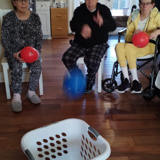 A group of people engaging in an indoor balloon activity, with a laundry basket on the floor.
