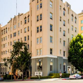 A multi-story apartment building on a street corner surrounded by trees.