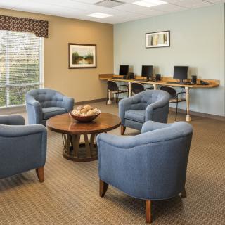 A cozy lounge area with blue chairs, a central round table, and a row of computers against the wall.