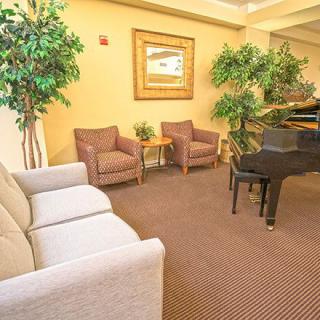 A cozy lobby area featuring chairs, a piano, and indoor plants.