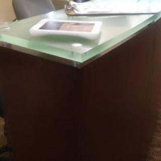 A modern office table featuring a glass top and wooden base.