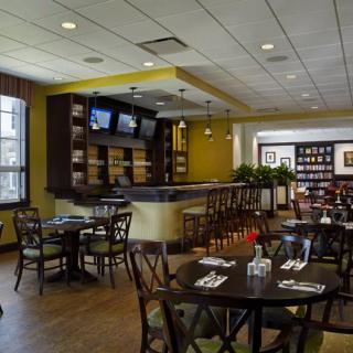 A modern restaurant interior featuring a dining area with tables, chairs, and a bar equipped with TV screens.