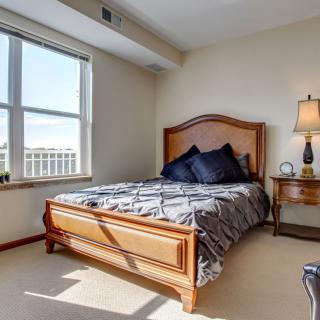 A cozy bedroom with a wooden bed frame, bedside table, and large window.