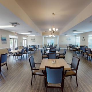 A spacious dining room with multiple tables and chairs, featuring large windows and elegant lighting.