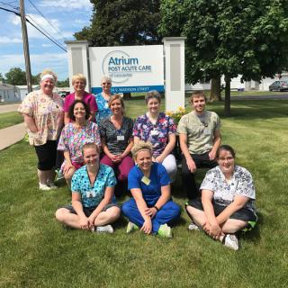 A group of people posing for a photo on a grassy area in front of a sign.