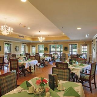 A well-decorated dining room with neatly arranged tables and chairs, featuring elegant chandeliers and large windows.