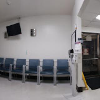 An empty hospital waiting room with blue chairs and a television mounted on the wall.