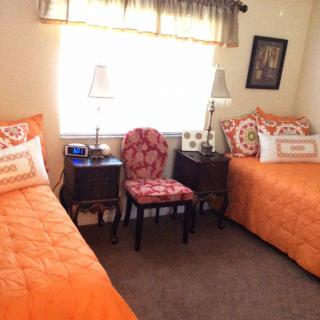 A cozy bedroom with two twin beds featuring orange bedding, a chair between them, and lamps on side tables.