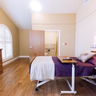 A modern bedroom interior featuring a hospital bed, wooden floors, and a window with shutters.