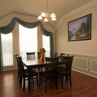 A well-appointed dining room featuring a wooden table with chairs, a chandelier, elegant window drapes, and an artwork on the wall.