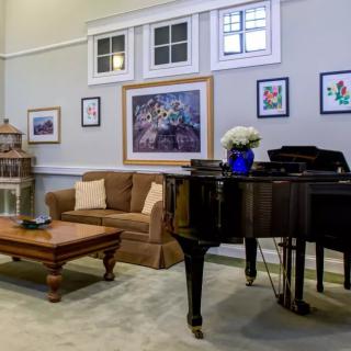 A cozy living room featuring a grand piano, comfortable couch, and various artworks on the walls.