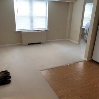An empty living room with carpet and hardwood flooring, featuring a large window.