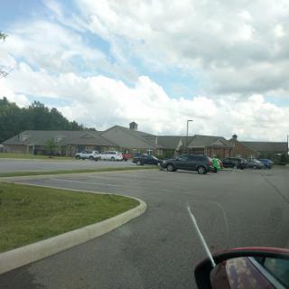 A view of a parking lot with several vehicles and a building under a cloudy sky.