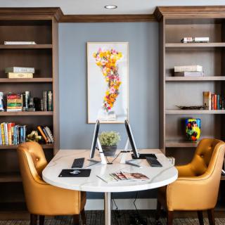 A cozy office space with a round desk, two leather chairs, and bookshelves filled with books.
