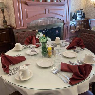 A formally set round dining table with red napkins, white dishes, and a floral centerpiece.