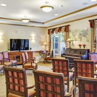 A well-furnished meeting room with chairs arranged in rows, a television, and a piano.