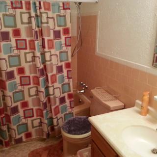 A bathroom with colorful square-patterned shower curtain and peach-colored tiles.