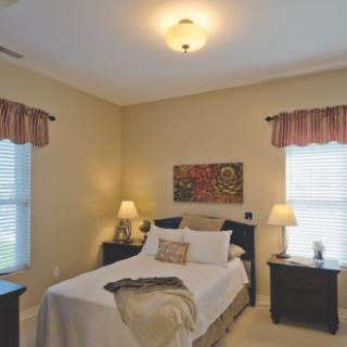 A cozy bedroom featuring a neatly made bed with bedside lamps and tasteful artwork.