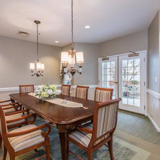 A well-appointed dining room featuring a long table surrounded by chairs, illuminated by elegant chandeliers.