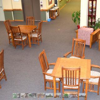 A quiet library reading area with wooden tables and chairs on a carpeted floor.