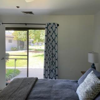 A cozy bedroom with a large window and stylish curtains, featuring a neatly made bed and a lamp on the side table.
