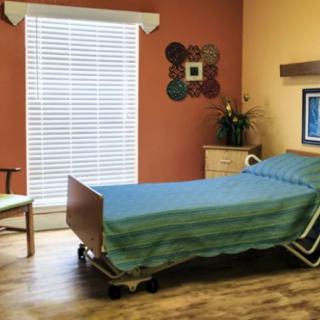 A hospital room with a single bed and a window, featuring warm colored walls.