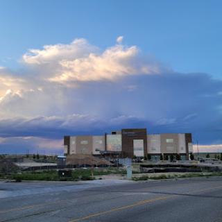 A modern building under a dramatic sky with fluffy clouds, showcasing an expansive landscape.