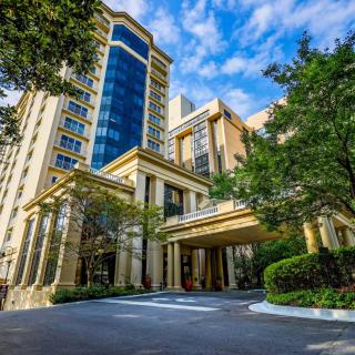 A modern hotel building with a grand entrance, surrounded by trees under a clear blue sky.