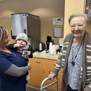 A heartwarming moment shared between a caregiver, an elderly woman, and a baby, highlighting the joy of connection across generations.