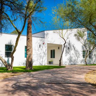 A modern white house with a driveway and surrounded by trees.