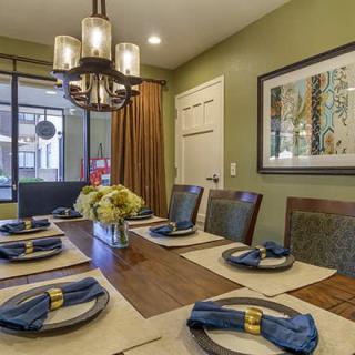 A modern dining room featuring an elegantly set table with blue napkins and a stylish chandelier overhead.