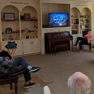 A cozy living room with people watching television and shelves filled with books.