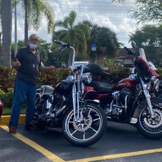 A person stands next to two parked motorcycles in a parking lot on a sunny day.