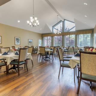 A spacious dining room with elegant tables and chairs, featuring large windows and a chandelier.