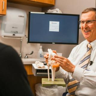 A doctor explains a knee model to a patient during a medical consultation in an office setting.