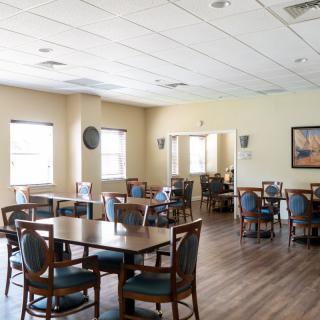 An empty dining area with tables and chairs, featuring large windows and a wooden floor.