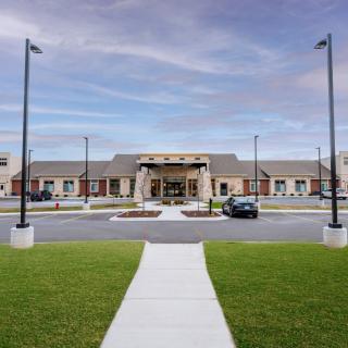 A modern building with a parking lot and neatly landscaped surroundings under a cloudy sky.