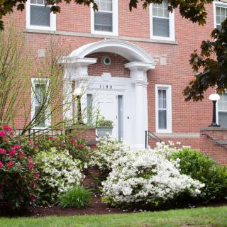 A brick building entrance surrounded by blooming flowers and bushes.