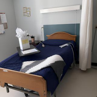 An empty hospital room with a neatly made bed and a gift bag on the tray table.