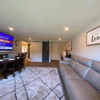 A modern living room featuring a large sofa, wall-mounted television, dining table, and stylish decor.