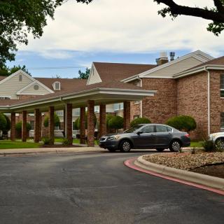 A residential building with a brick facade and covered entrance, featuring parked cars along the driveway.