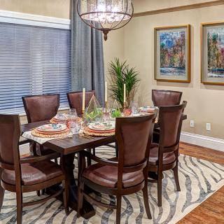A cozy dining room with a wooden table, surrounded by chairs, adorned with elegant decor and paintings on the wall.